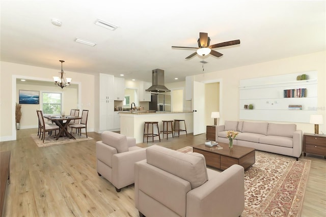 living room featuring ceiling fan with notable chandelier, sink, and light hardwood / wood-style flooring