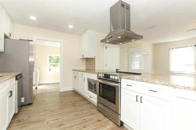 kitchen with stainless steel appliances, white cabinetry, light stone countertops, island range hood, and light hardwood / wood-style flooring