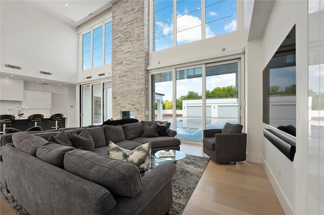 living room with light wood-type flooring, a towering ceiling, and a fireplace