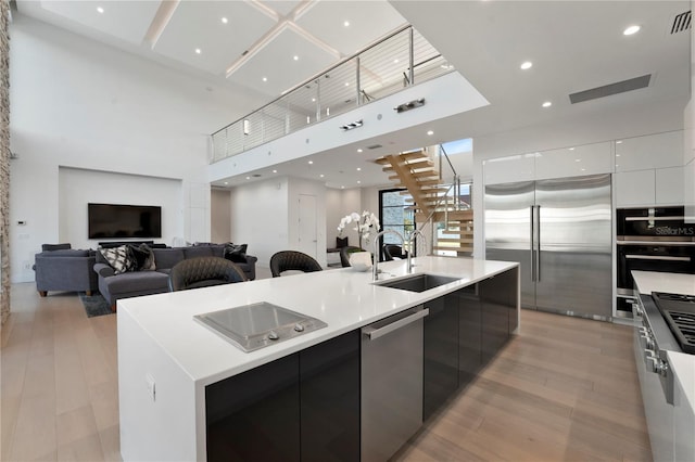 kitchen with appliances with stainless steel finishes, sink, a large island with sink, light hardwood / wood-style flooring, and white cabinetry