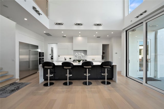 kitchen featuring a high ceiling, white cabinetry, stainless steel built in fridge, and a kitchen breakfast bar