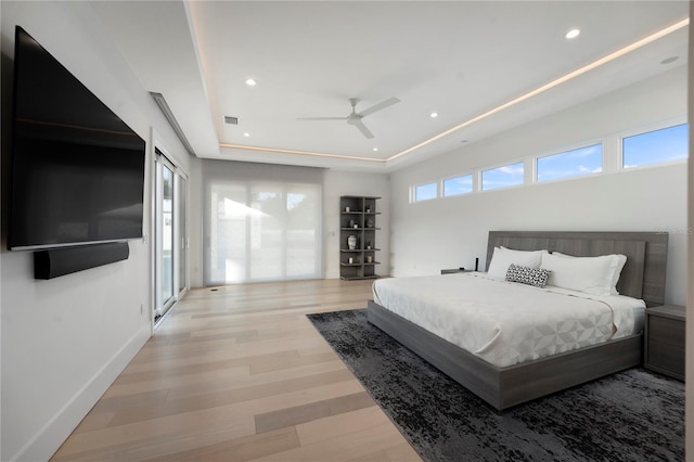 bedroom with a tray ceiling, light hardwood / wood-style flooring, and ceiling fan