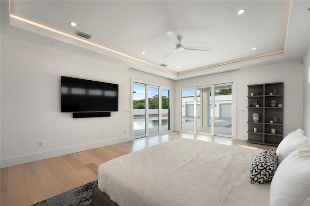 bedroom featuring ceiling fan, access to exterior, light wood-type flooring, and a tray ceiling