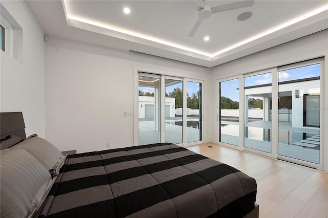 bedroom featuring a tray ceiling, access to exterior, ceiling fan, and light hardwood / wood-style flooring