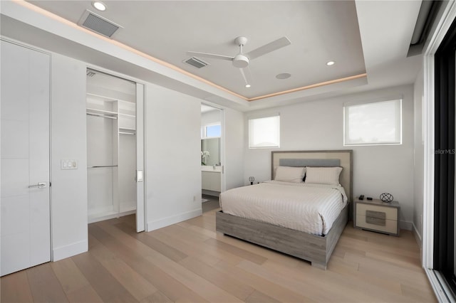 bedroom with connected bathroom, ceiling fan, a raised ceiling, light hardwood / wood-style floors, and a closet