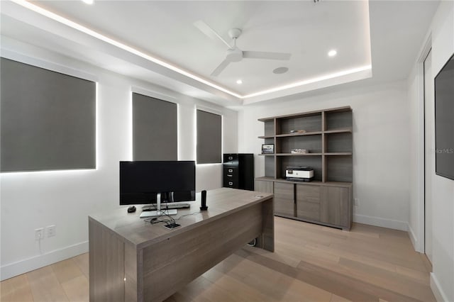 office featuring ceiling fan, a tray ceiling, and light hardwood / wood-style flooring