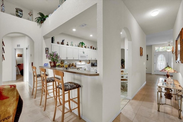 kitchen with white appliances, white cabinets, kitchen peninsula, a kitchen bar, and light tile floors