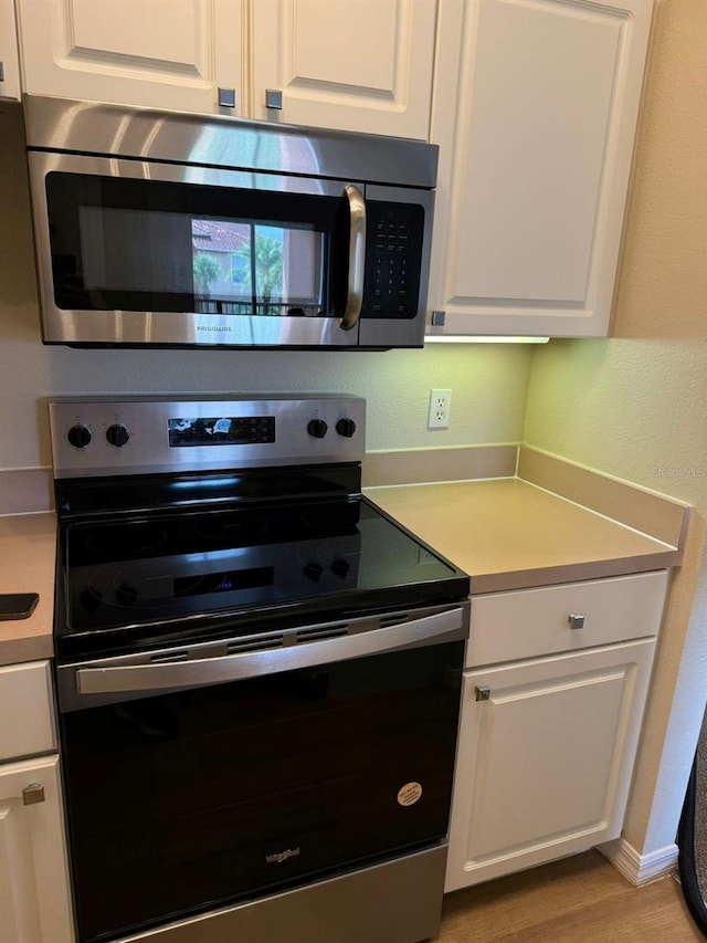 kitchen with stainless steel appliances, white cabinetry, and light wood-type flooring