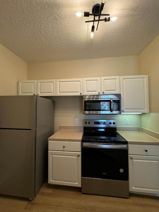 kitchen with wood-type flooring, appliances with stainless steel finishes, white cabinets, and a textured ceiling