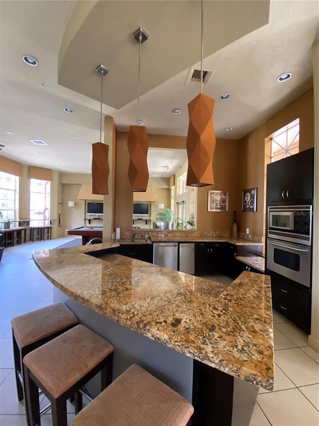 kitchen featuring hanging light fixtures, light tile patterned flooring, appliances with stainless steel finishes, and kitchen peninsula