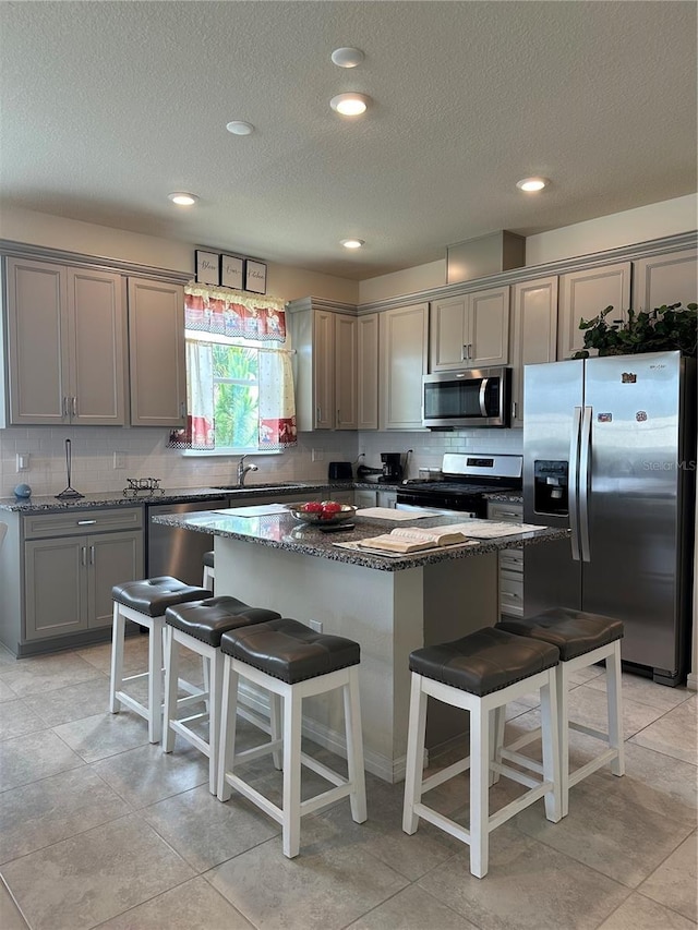 kitchen with stainless steel appliances, a kitchen breakfast bar, a center island, and dark stone counters