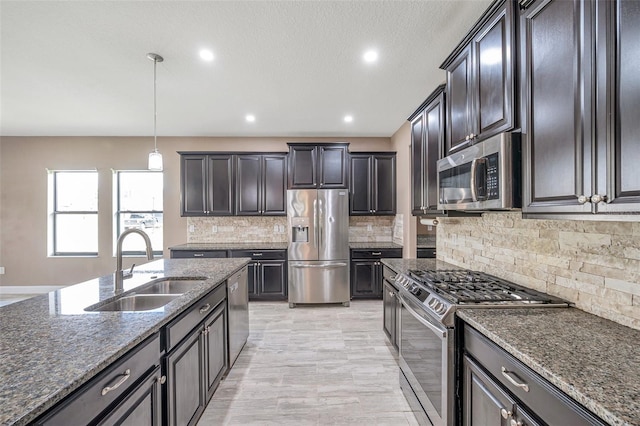 kitchen with dark stone counters, hanging light fixtures, appliances with stainless steel finishes, and a sink