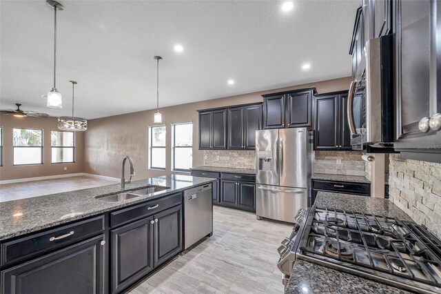 kitchen with dark cabinets, dark stone countertops, hanging light fixtures, stainless steel appliances, and a sink