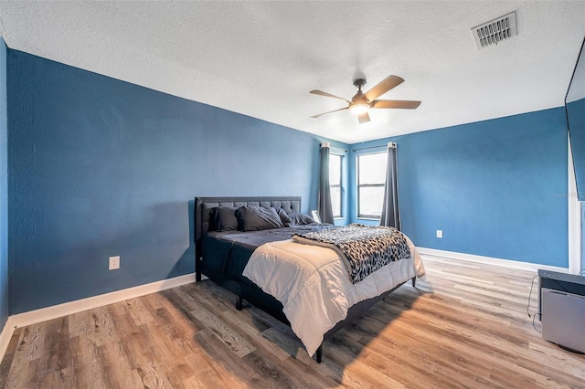 bedroom featuring a textured ceiling, ceiling fan, wood finished floors, visible vents, and baseboards