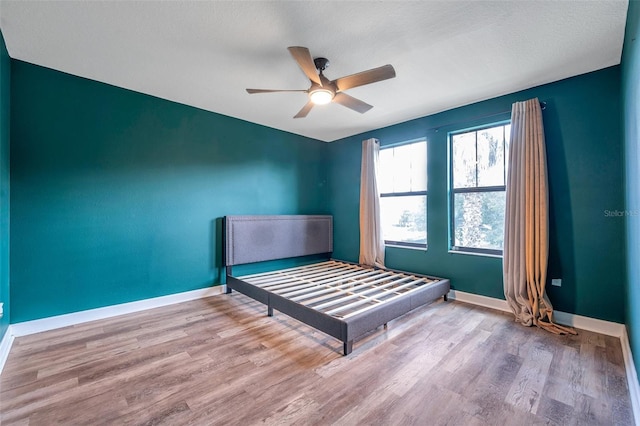 bedroom with light wood finished floors, a ceiling fan, and baseboards