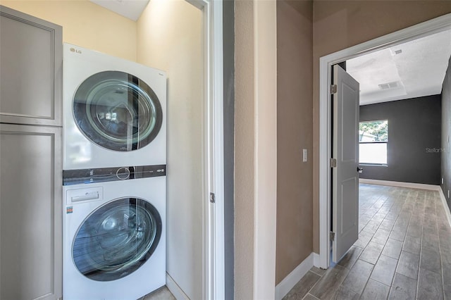 washroom with wood finish floors, visible vents, stacked washer / dryer, laundry area, and baseboards