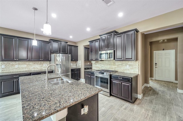 kitchen with stainless steel appliances, visible vents, hanging light fixtures, a sink, and an island with sink