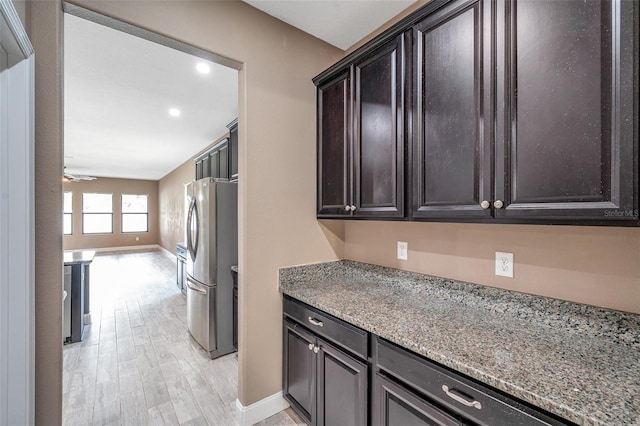 kitchen featuring ceiling fan, light stone counters, light wood-style floors, dark brown cabinets, and freestanding refrigerator