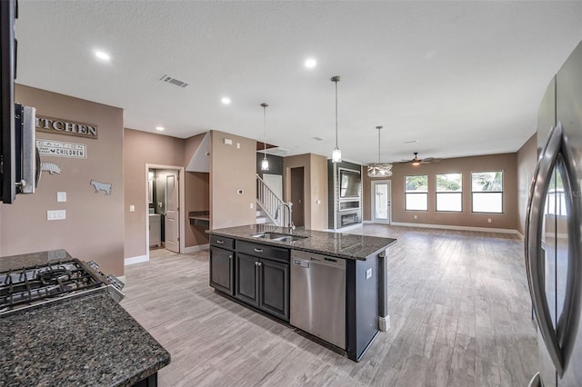 kitchen featuring stainless steel appliances, a sink, open floor plan, hanging light fixtures, and a center island with sink