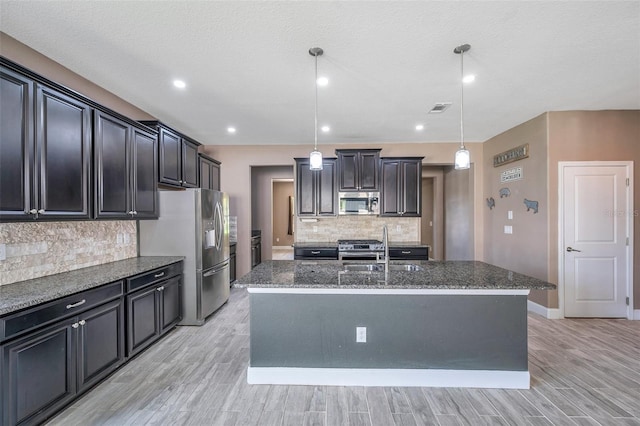 kitchen with stainless steel appliances, decorative light fixtures, and a center island with sink