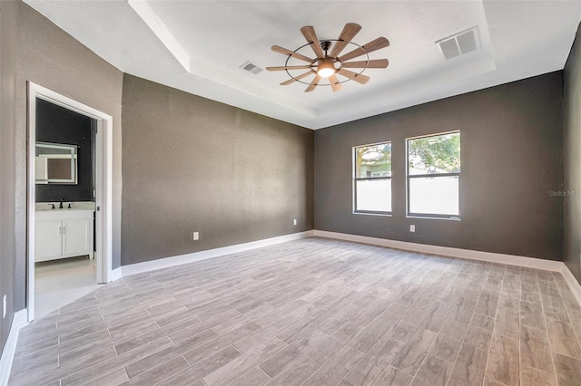 empty room with light wood-type flooring, a raised ceiling, visible vents, and baseboards