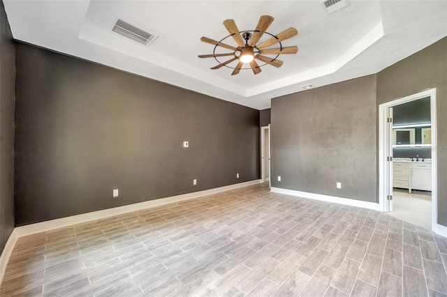 spare room with ceiling fan, a raised ceiling, visible vents, and baseboards