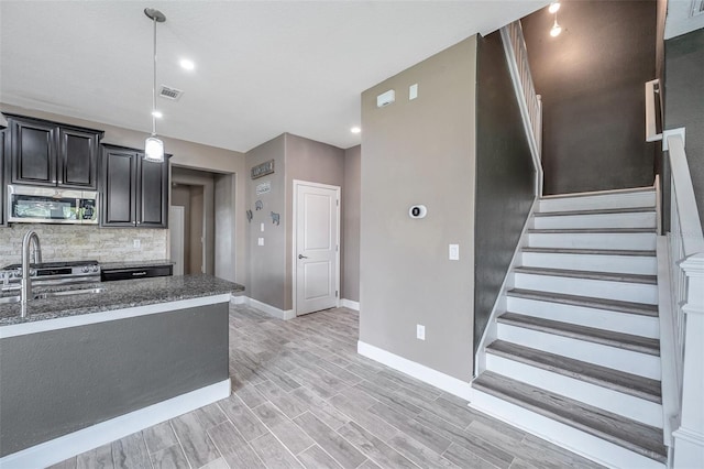 kitchen featuring dark cabinets, visible vents, hanging light fixtures, backsplash, and stainless steel microwave