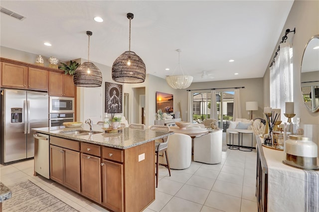 kitchen with hanging light fixtures, stainless steel appliances, a kitchen island with sink, sink, and light tile flooring