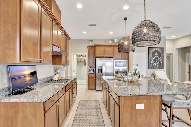 kitchen featuring appliances with stainless steel finishes, a kitchen island with sink, a breakfast bar area, pendant lighting, and light tile floors