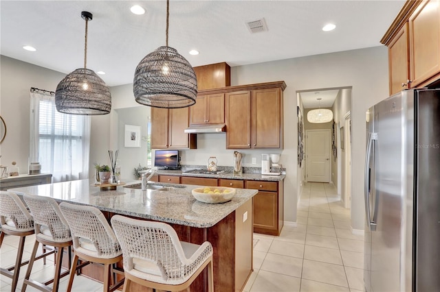 kitchen with stainless steel appliances, decorative light fixtures, light tile flooring, sink, and a kitchen island with sink