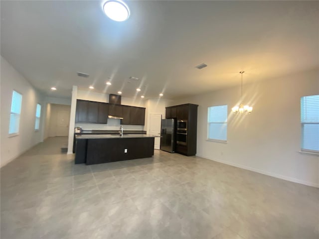 kitchen with stainless steel fridge, an inviting chandelier, an island with sink, sink, and light tile floors