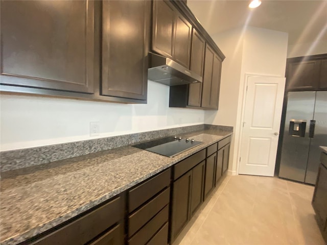 kitchen featuring stainless steel refrigerator with ice dispenser, wall chimney range hood, dark brown cabinetry, black electric cooktop, and light tile floors