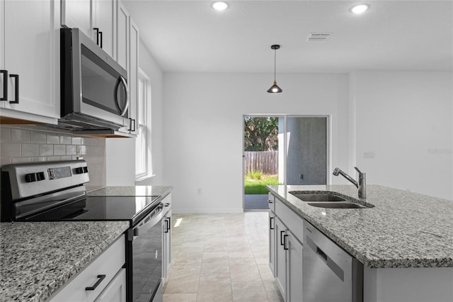 kitchen with light stone countertops, a kitchen island with sink, hanging light fixtures, stainless steel appliances, and sink