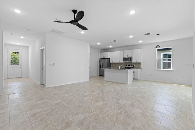 interior space with white cabinets, appliances with stainless steel finishes, light stone countertops, ceiling fan, and a kitchen island with sink