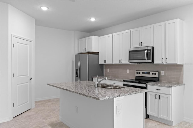 kitchen with a center island with sink, appliances with stainless steel finishes, sink, white cabinetry, and light stone counters