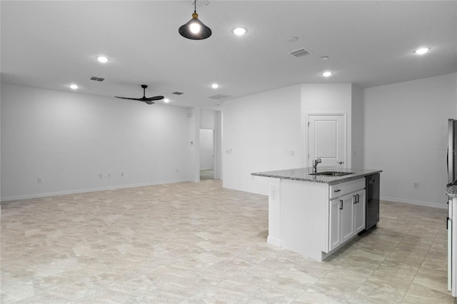 kitchen featuring a center island with sink, sink, white cabinetry, ceiling fan, and stone counters