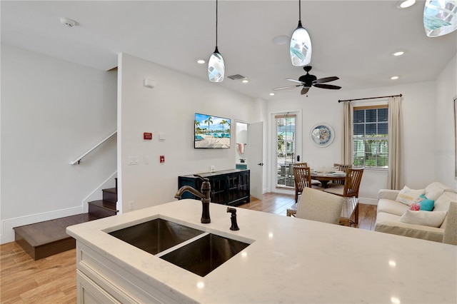 kitchen featuring ceiling fan, light hardwood / wood-style flooring, pendant lighting, light stone counters, and sink