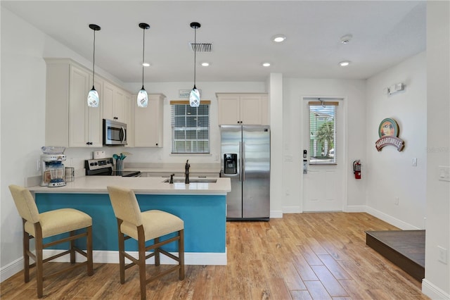 kitchen with light hardwood / wood-style floors, hanging light fixtures, kitchen peninsula, and stainless steel appliances