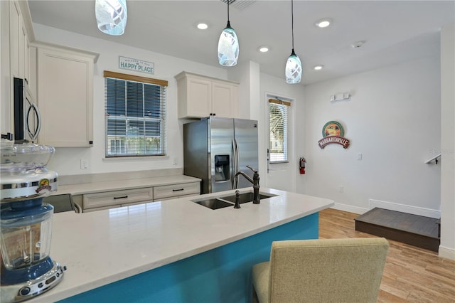 kitchen with light wood-type flooring, hanging light fixtures, sink, white cabinetry, and appliances with stainless steel finishes