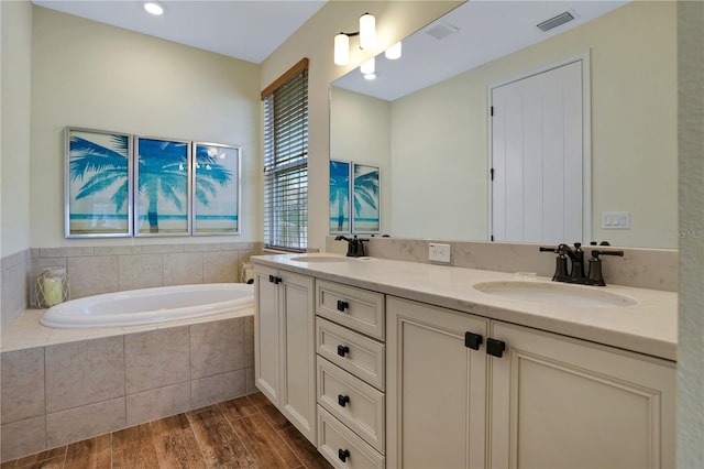 bathroom with a relaxing tiled bath, hardwood / wood-style floors, double sink, and large vanity