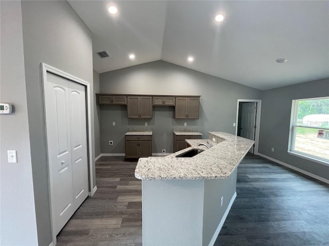 kitchen with lofted ceiling, a center island with sink, sink, dark hardwood / wood-style floors, and light stone countertops