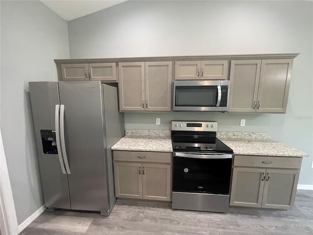 kitchen featuring light stone countertops, appliances with stainless steel finishes, gray cabinetry, light hardwood / wood-style flooring, and lofted ceiling