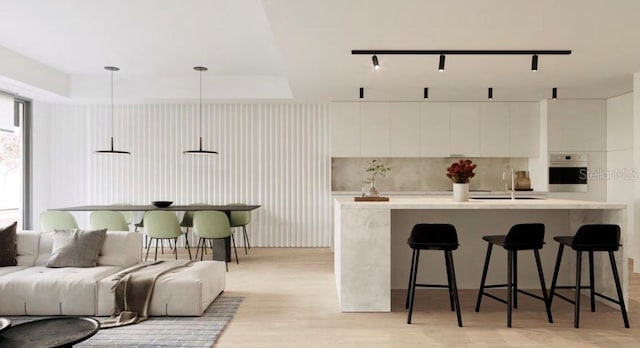 kitchen with light hardwood / wood-style floors, stainless steel oven, decorative light fixtures, backsplash, and white cabinets