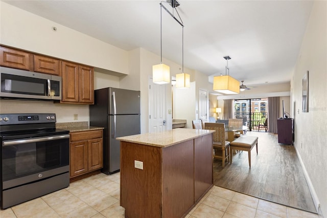 kitchen featuring hanging light fixtures, ceiling fan, light stone countertops, light wood-type flooring, and stainless steel appliances