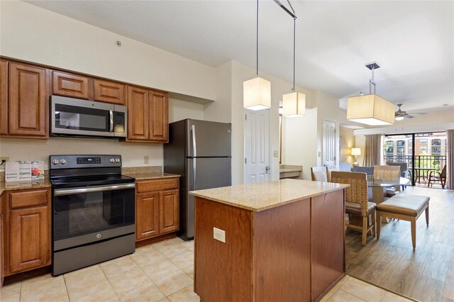 kitchen with light stone countertops, appliances with stainless steel finishes, a kitchen island, hanging light fixtures, and light hardwood / wood-style flooring