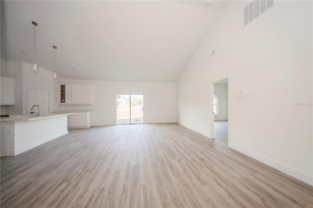 unfurnished living room with sink, light hardwood / wood-style floors, and high vaulted ceiling