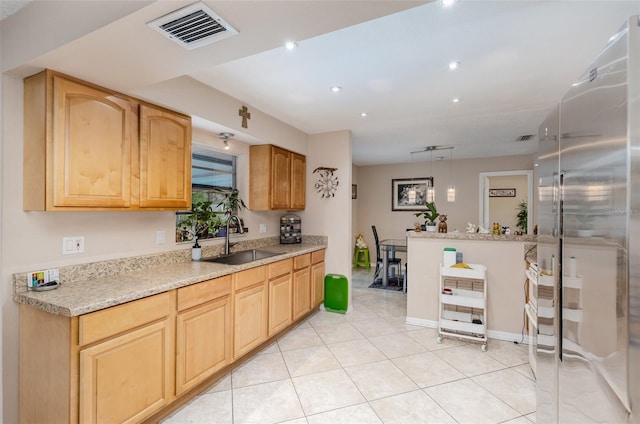 kitchen featuring light stone countertops, high end refrigerator, decorative light fixtures, sink, and light tile floors