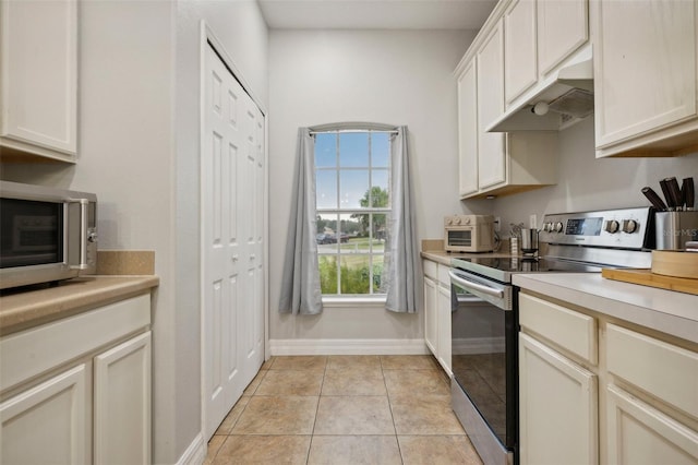 kitchen with stainless steel appliances, white cabinetry, light tile flooring, and premium range hood