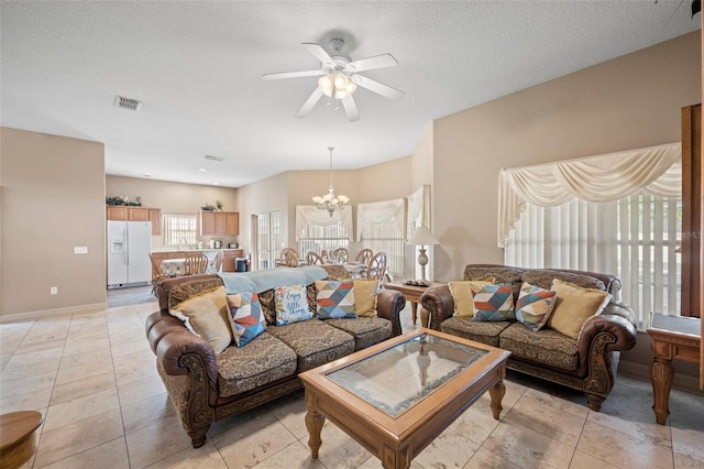 tiled living room featuring a textured ceiling and ceiling fan with notable chandelier