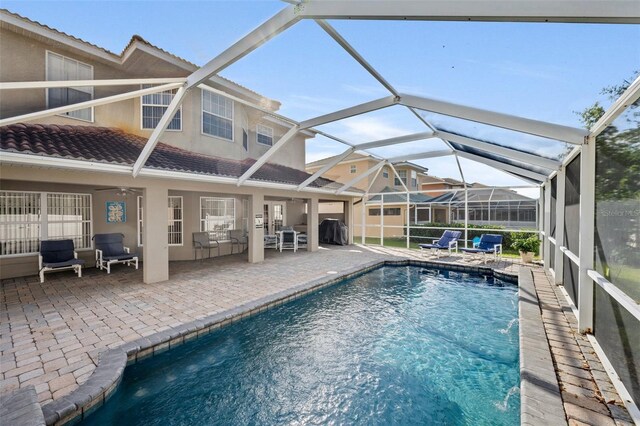 view of pool featuring glass enclosure, grilling area, pool water feature, an outdoor hangout area, and a patio area